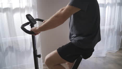 home-training-with-stationary-bicycle-man-is-spinning-pedals-keeping-fit-during-self-isolation-in-pandemic-time-physical-activity-at-middle-age